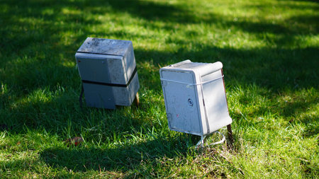 Two gray utility boxes secured with straps on green grass under sunlight