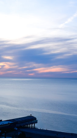 Coastal landscape featuring a pier and tranquil ocean under a colorful sunset skyの写真素材