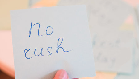 Hand holding note with handwritten message no rush on pastel background.