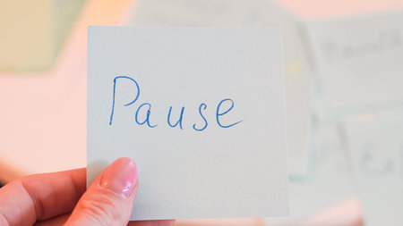 A hand with pink nail polish holds a note that says Pause in blue ink against a soft background