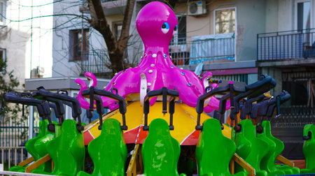 Bright pink octopus ride with green seats in a playground surrounded by buildingsの写真素材