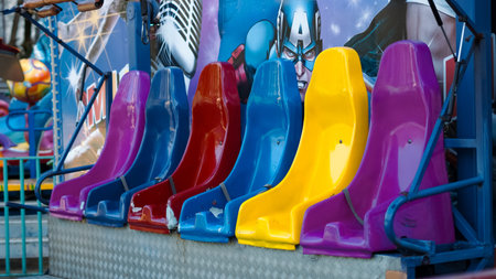 Brightly colored seats in red, blue, yellow, and purple arranged in a row at an amusement parkの写真素材