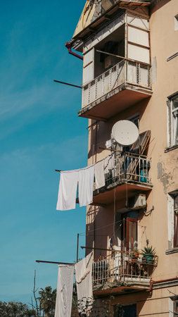 Multi-story apartment building with white laundry hanging from balconies against a clear blue skyの写真素材