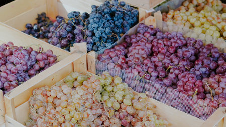 Variety of grapes including green, red, and black in wooden crates at a marketの写真素材