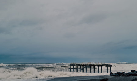 Ocean waves crash against a wooden pier under a cloudy sky with dark storm clouds