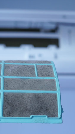 Close-up of a hand holding a dirty air conditioning filter with the unit in backgroundの写真素材