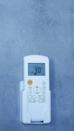 Air conditioning remote control displaying temperature mounted on a gray wall