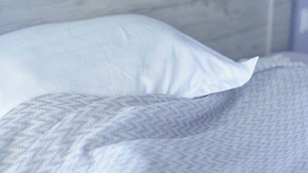 White pillow rests on a gray chevron-patterned blanket on a bed with a wooden headboard
