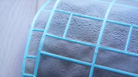 Close-up view of a dirty air filter with a blue frame resting on a wooden surface