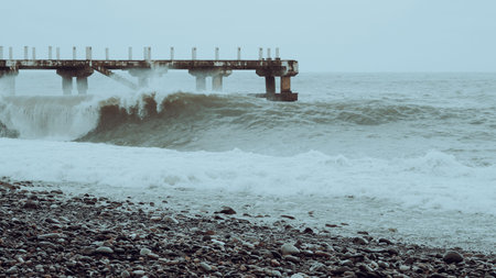 Ocean waves break on rocky beach with a wooden pier visible in the background