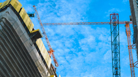 Two construction cranes operate above a building under construction against a blue sky