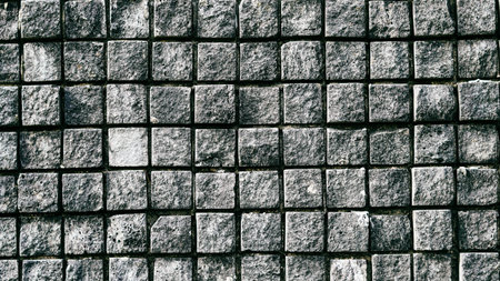 Close-up view of a textured stone wall featuring square gray stones arranged in a gridの写真素材