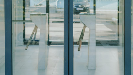 Turnstiles positioned at the entrance of a contemporary building with glass doors and pavement