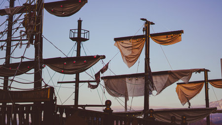 Tall masts of a pirate ship with sails and rigging illuminated by sunset sky colors