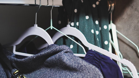 Various garments hanging on white hangers in a closet with polka dot and patterned clothing