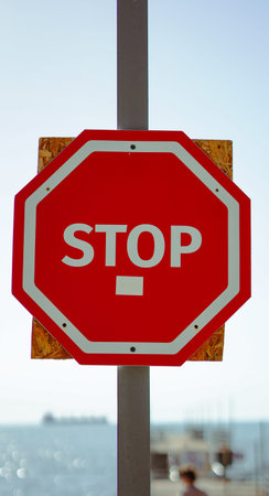 A red octagonal stop sign mounted on a wooden backing near the coast.