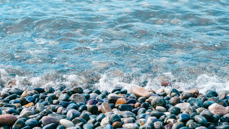 Sea waves washing over wet colorful pebbles on a beach.
