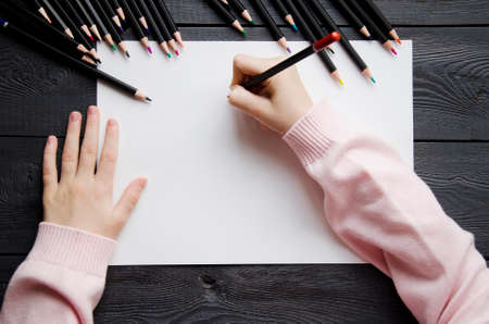The childs hands on a white sheet of paper next to pencils. Mockupの写真素材