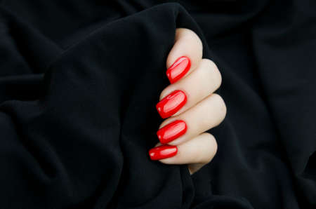 A womans hand with a red manicure on a black backgroundの写真素材