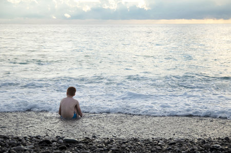 Happy child plays with sea waves. Child splashes in water on shore. Kids summer vacation.の写真素材