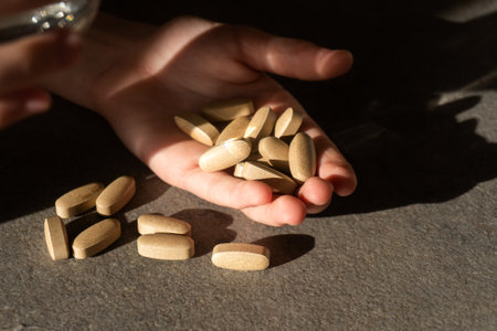 pills and a glass of water in a hand with shadow and glare of the sunの写真素材