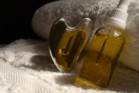 Stainless steel gua sha tool, bottle with oil on a beige towel.の写真素材