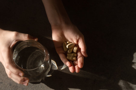 pills and a glass of water in hands with shadow and glare of the sunの写真素材