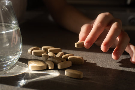 pills and a glass of water in children's hands with shadow and glare of the sunの写真素材