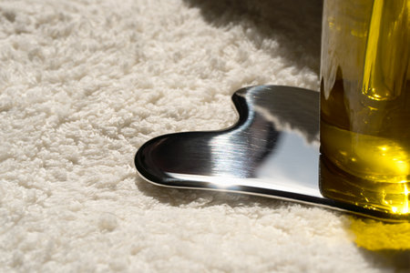 Stainless steel gua sha tool, bottle with oil on a beige towel.の写真素材