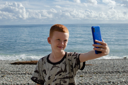 Teenager uses a phone on the beach against the backdrop of the sea or oceanの写真素材