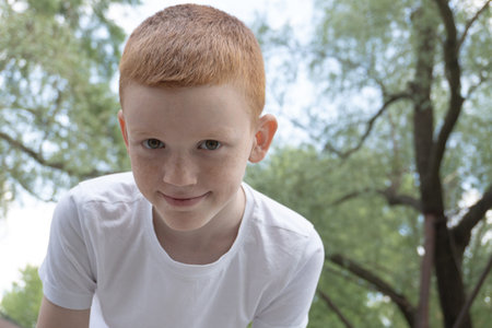 portrait of a red-haired boy against the background of the sky and treesの写真素材