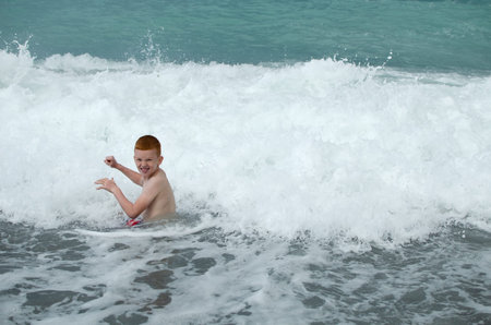 Happy child plays with sea waves. Child splashes in water on shore. Kids summer vacation.