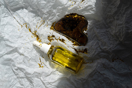 A bottle of oil and a gua sha scraper lie on a white background with glitter.の写真素材