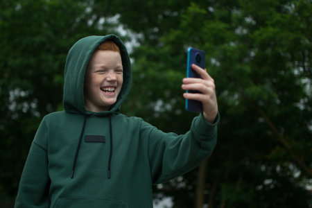 A boy in the park communicates on the phone, takes a selfie on the phoneの写真素材