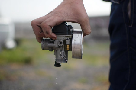 A mechanic holds a carburetor in his hands. Pit stop. Preparing the car for a sports raceの写真素材