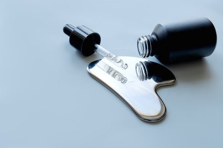Stainless steel gua sha tool and a pipette with a cosmetic product, space for text.の写真素材