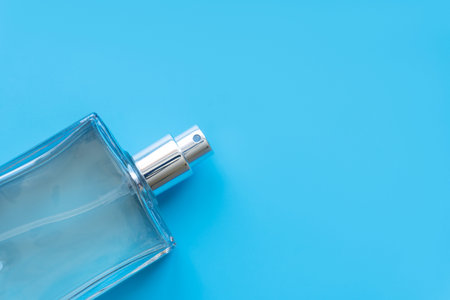 Transparent glass cosmetic bottle for perfume on a blue surface. Top view. Background for your...