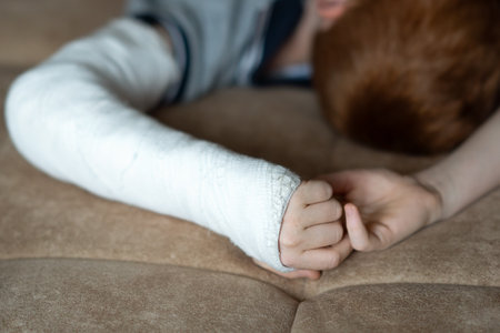 A teenage boy with a broken arm wrapped in a white plaster cast resting on the bedの写真素材