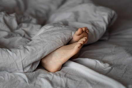 Feet under a light blanket on the bed, soft focus background. Concept of health.