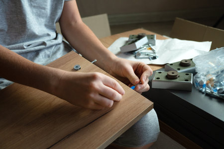 Cropped hand of a child assembling furniture according to instructions, using different tools. Active help around the house, a man's hobby.の写真素材