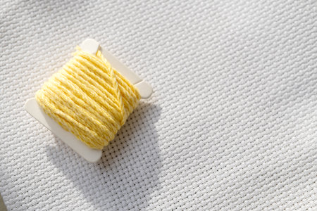 A spool with yellow threads for embroidery on a white canvasの写真素材