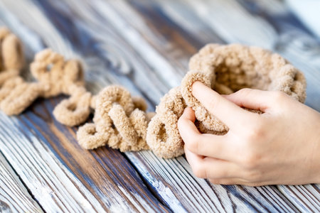 The fingers of a small child are knitting on brown yarn. Childrens hobby. The girl sits holding a woolen thread in her hands.の写真素材
