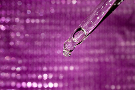Glass pipette with facial serum on violet background. Essential oil close-up in a pipette. A skin care product with hyaluronic acid in a pipette.の写真素材