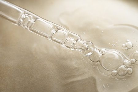 Glass pipette with facial serum on on brown background. Essential oil close-up in a pipette. A skin care product with hyaluronic acid in a pipette.の写真素材