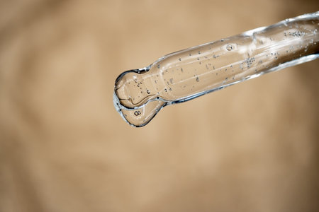 Glass pipette with facial serum on on brown background. Essential oil close-up in a pipette. A skin...