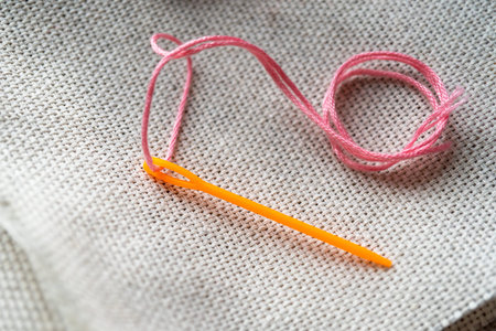 A plastic needle with a threaded floss on an embroidery canvas. Close-up