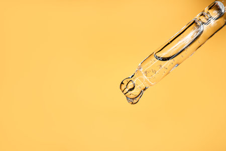 Glass pipette with facial serum on a light background. Essential oil close-up in a pipette. A skin...