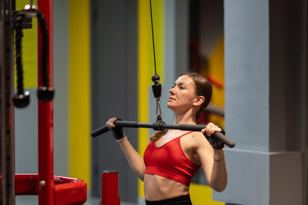 Dedicated serious fit woman with sweat doing exercises, working out on Lat pulldown machine in...