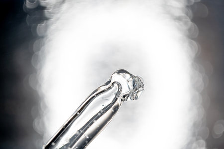 Glass pipette with facial serum in black and white background. Essential oil close-up in a pipette. A skin care product with hyaluronic acid in a pipette.の写真素材