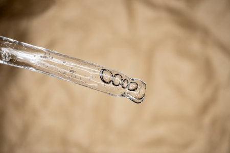 Glass pipette with facial serum on on brown background. Essential oil close-up in a pipette. A skin care product with hyaluronic acid in a pipette.の写真素材